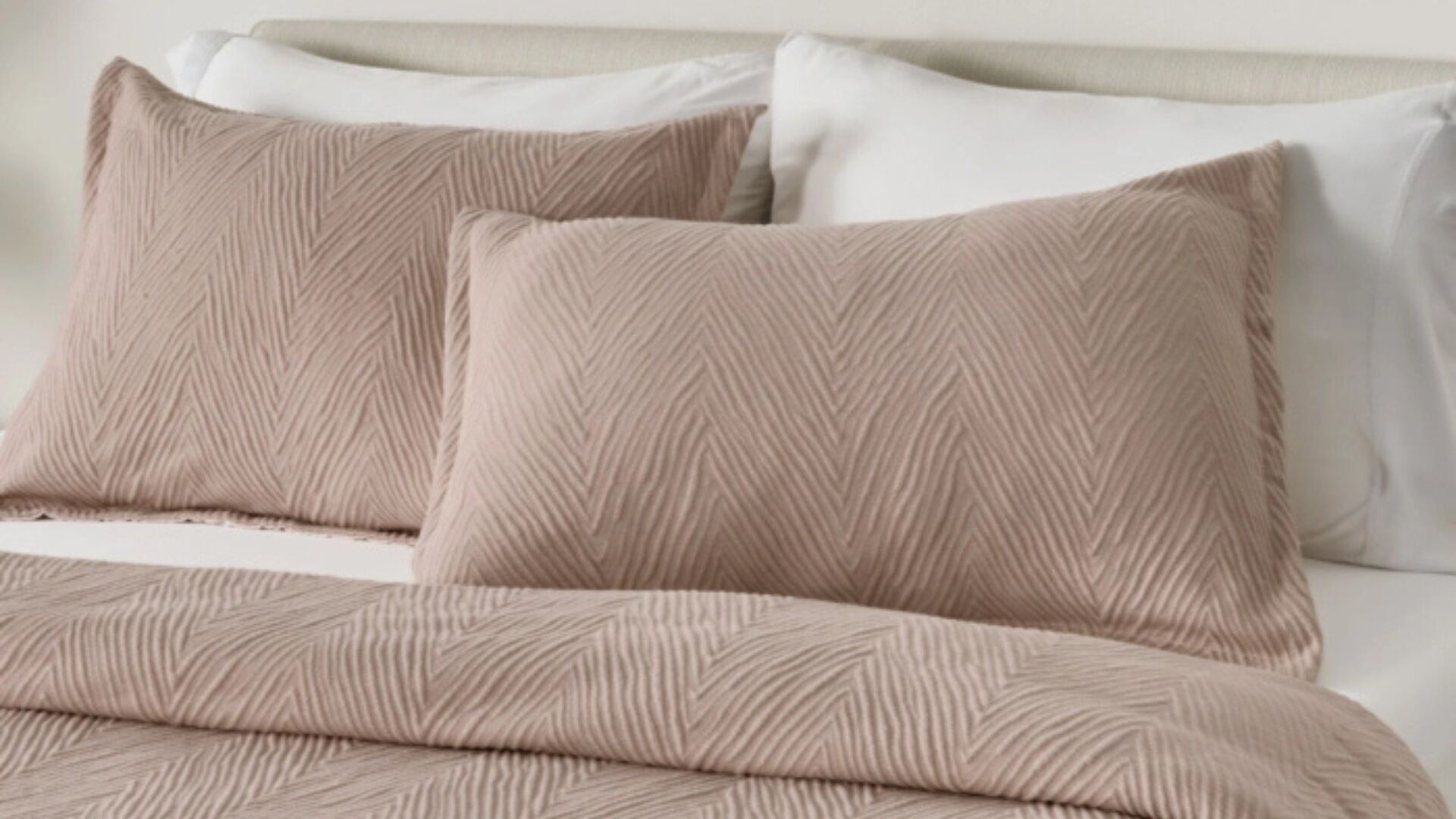 Cozy bed with taupe geometric coverlet, matching pillows, white sheets, and minimal headboard.