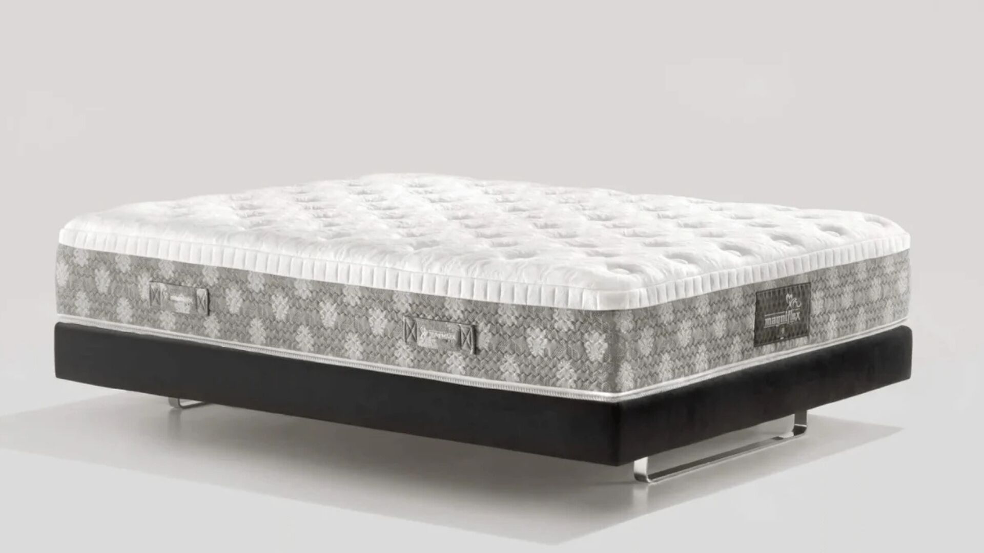 Plush white mattress with geometric sides on sleek black platform bed frame with metallic legs.